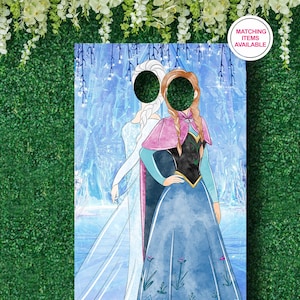 Puede incluir: Un recorte de cart&oacute;n de Elsa y Anna de Frozen, con espacios para las caras. El recorte est&aacute; sobre un fondo azul y blanco con una escena invernal. El texto "Art&iacute;culos a juego disponibles" est&aacute; en un c&iacute;rculo rosa en la esquina superior derecha.