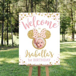 Pu&ograve; includere: Benvenuti al 1&deg; compleanno di Isabella, un cartello con un design di orecchie di Topolino rosa e oro. Il cartello ha una cornice per foto con una foto di una bambina. Lo sfondo &egrave; composto da coriandoli rosa e oro.