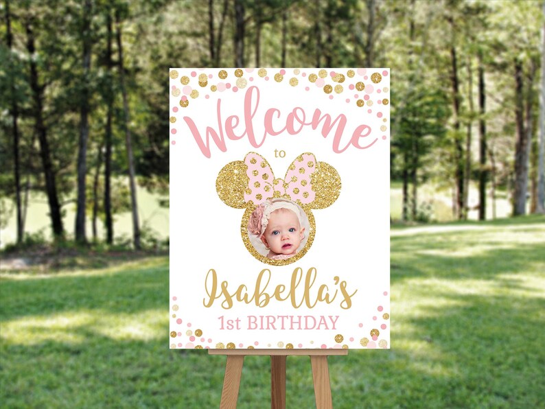 Pu&ograve; includere: Benvenuti al 1&deg; compleanno di Isabella, un cartello con un design di orecchie di Topolino rosa e oro. Il cartello ha una cornice per foto con una foto di una bambina. Lo sfondo &egrave; composto da coriandoli rosa e oro.