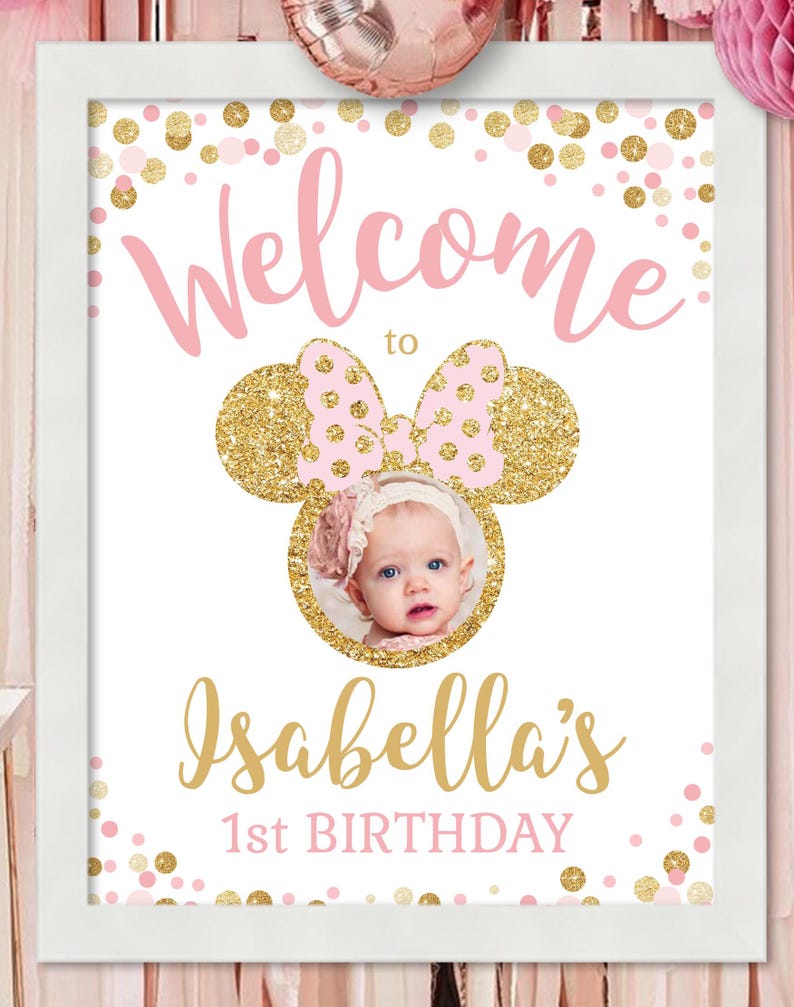 Pu&ograve; includere: Un cartello di benvenuto rosa e oro con una cornice per foto a forma di testa di Minnie Mouse. Il cartello dice "Benvenuti al 1&deg; compleanno di Isabella" con coriandoli rosa e oro sullo sfondo.