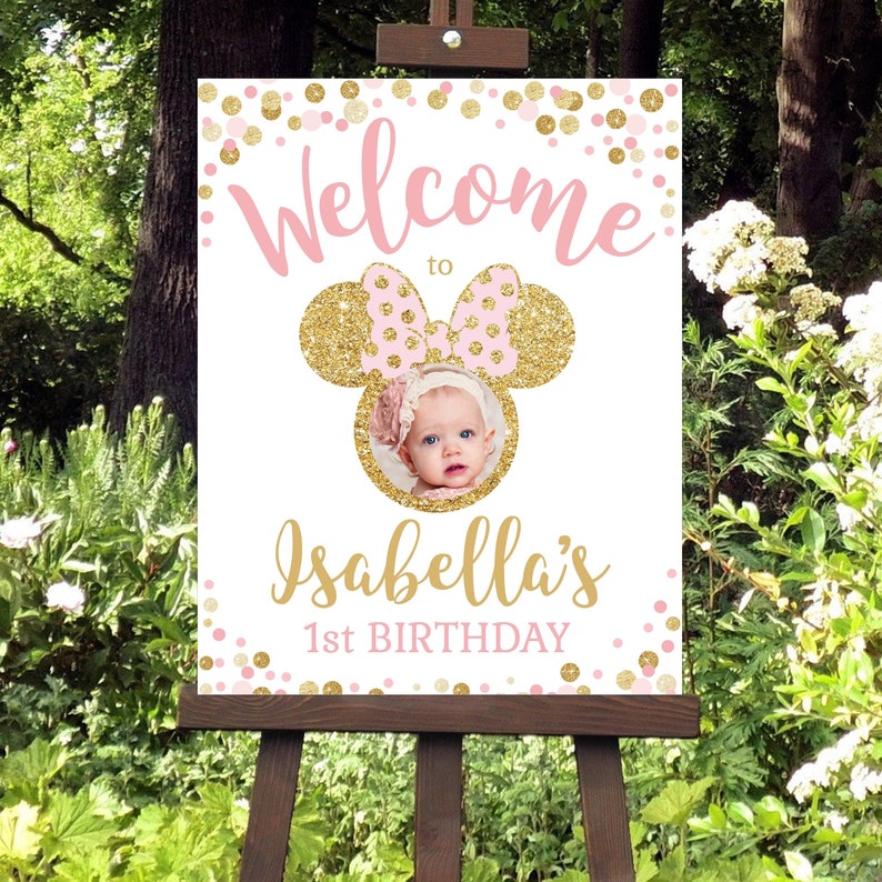 Pu&ograve; includere: Benvenuti al 1&deg; compleanno di Isabella con un design di orecchie di Minnie Mouse in glitter rosa e oro e una foto di una bambina. Il cartello ha uno sfondo di coriandoli rosa e oro.