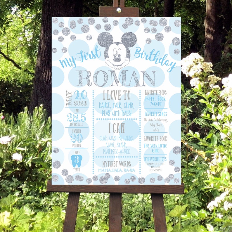 K&ouml;nnte beinhalten: Ein blaues und silbernes erstes Geburtstagsschild mit einer Mickey Mouse Figur. Das Schild enth&auml;lt den Namen des Kindes, Roman, und Details &uuml;ber sein erstes Jahr, einschlie&szlig;lich seiner Gr&ouml;&szlig;e, seines Gewichts, seiner Lieblingsessen und seiner ersten Worte.