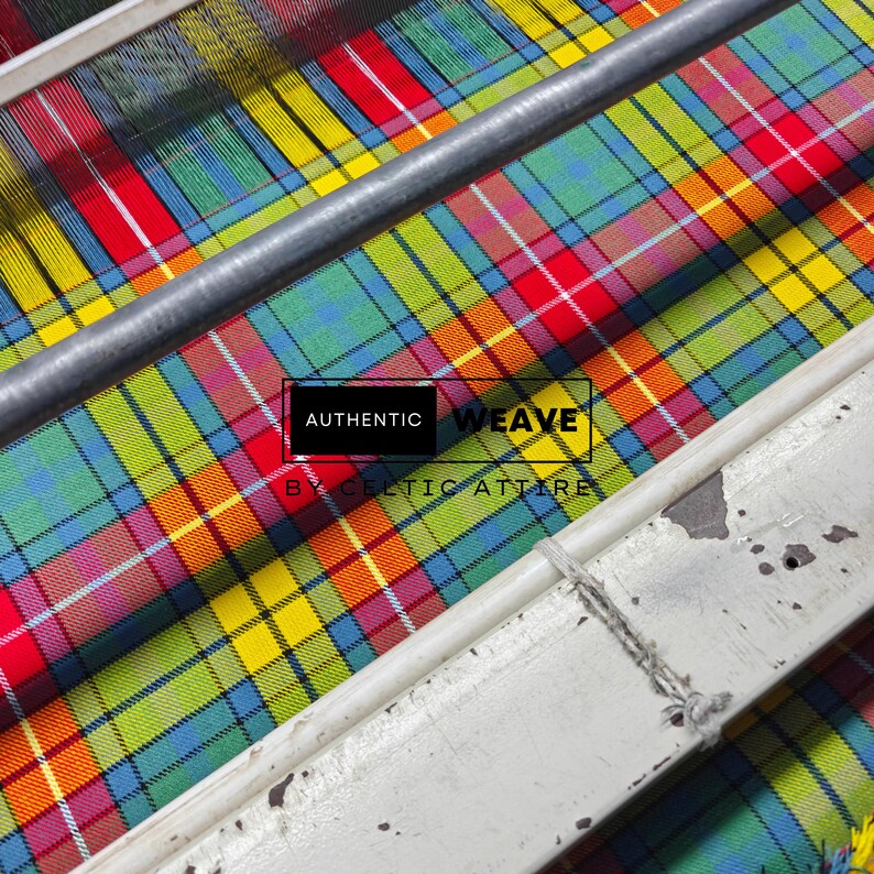 K&ouml;nnte beinhalten: Nahaufnahme eines bunten Tartan-Stoffs in Rot, Gelb, Gr&uuml;n und Blau auf einem Webstuhl. Metall- und wei&szlig;e Holzteile sind zu sehen. Der Text "AUTHENTIC WEAVE BY CELTIC ATTIRE" ist auf dem Stoff abgebildet.