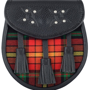 May include: A black leather sporran with three black tassels and a red, yellow, and green tartan design. The sporran has a flap with a Celtic knot design and silver studs.