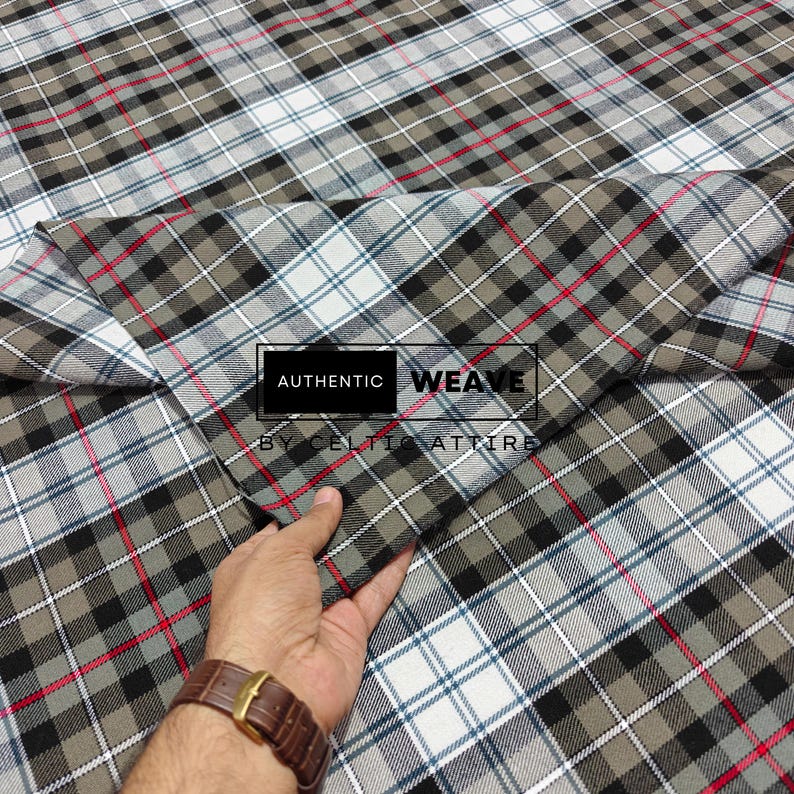 K&ouml;nnte beinhalten: Ein gefalteter Stoff mit Karomuster in Grau-, Schwarz-, Wei&szlig;- und Rott&ouml;nen. Der Stoff hat ein klassisches Karomuster. Der Text "AUTHENTIC WEAVE BY CELTIC ATTIRE" ist auf den Stoff gedruckt.