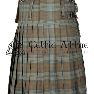 May include: A brown and green plaid kilt with black leather straps and buckles. The kilt is pleated and has a fringed edge. The text "Celtic Attire Kilts-Jackets-Accessories" is printed on the kilt.