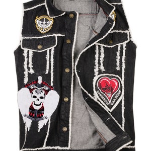 Peut inclure: Gilet en jean noir avec des surpiqûres blanches et plusieurs patchs. Les patchs représentent un crâne avec des ailes, un cœur avec un crâne et un symbole ailé avec le texte "Special Forces".