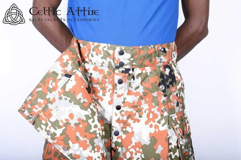 K&ouml;nnte beinhalten: Ein Tarnkilt mit orangefarbenen, gr&uuml;nen und wei&szlig;en Mustern. Der Kilt hat einen Knopfverschluss und eine Tasche an der Seite.
