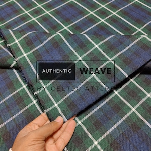 Op de afbeelding: Close-up van een groene, blauwe en witte geruite stof met de tekst "AUTHENTIC WEAVE BY CELTIC ATTIRE" erop gedrukt.