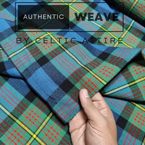 Puede incluir: Primer plano de una tela tartán azul, verde, roja y negra. La tela está doblada y una mano sostiene el borde. El texto "AUTHENTIC WEAVE BY CELTIC ATTIRE" está impreso en un rectángulo negro.