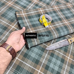 K&ouml;nnte beinhalten: Gr&uuml;n, braun und wei&szlig; karierter Stoff mit einem gelben Ma&szlig;band und einem silbernen und goldenen Messer. Der Stoff tr&auml;gt den Text "AUTHENTIC WEAVE BY CELTIC ATTIRE".