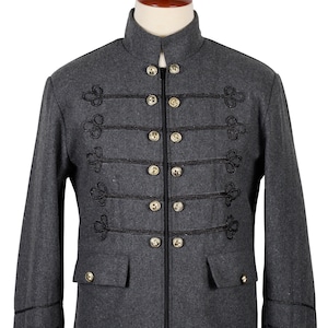 Könnte beinhalten: Eine graue Wolljacke mit Stehkragen, Reißverschluss und goldenen Knöpfen. Die Jacke hat einen schwarzen Besatz und dekorative Schlaufen an der Vorderseite.