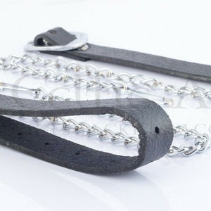 Pu&ograve; includere: Due cinturini in pelle nera con catena e ferramenta in metallo color argento. I cinturini hanno un'asola a un'estremit&agrave; e un anello di metallo all'altra. La catena &egrave; attaccata all'anello e all'asola.