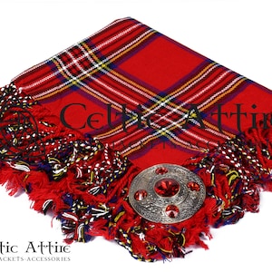 May include: Red tartan kilt pin with a silver and red metal kilt pin with a red stone in the center. The kilt pin is on a red tartan fabric with fringe.