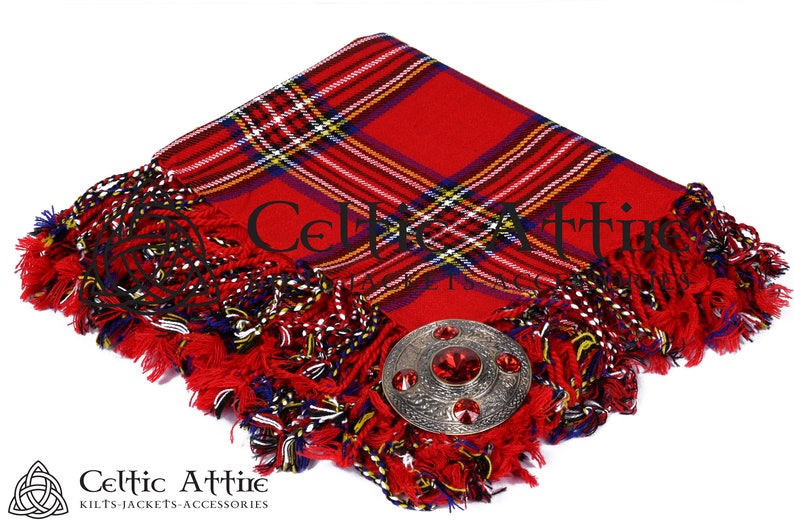 May include: Red tartan kilt pin with a silver and red metal kilt pin with a red stone in the center. The kilt pin is on a red tartan fabric with fringe.
