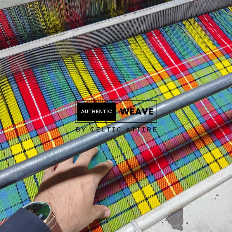 K&ouml;nnte beinhalten: Ein mehrfarbiger Stoff im Webprozess auf einem Webstuhl. Der Stoff weist eine lebendige Mischung aus Rot, Gelb, Blau und Gr&uuml;n auf. Der Text "AUTHENTIC WEAVE BY CELTIC ATTIRE" ist auf dem Stoff zu sehen.