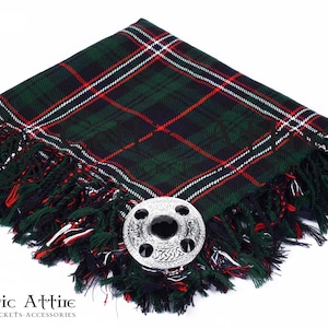 May include: A green, red, and white tartan kilt pin with a silver Celtic knot design. The pin is on a green, red, and white kilt.