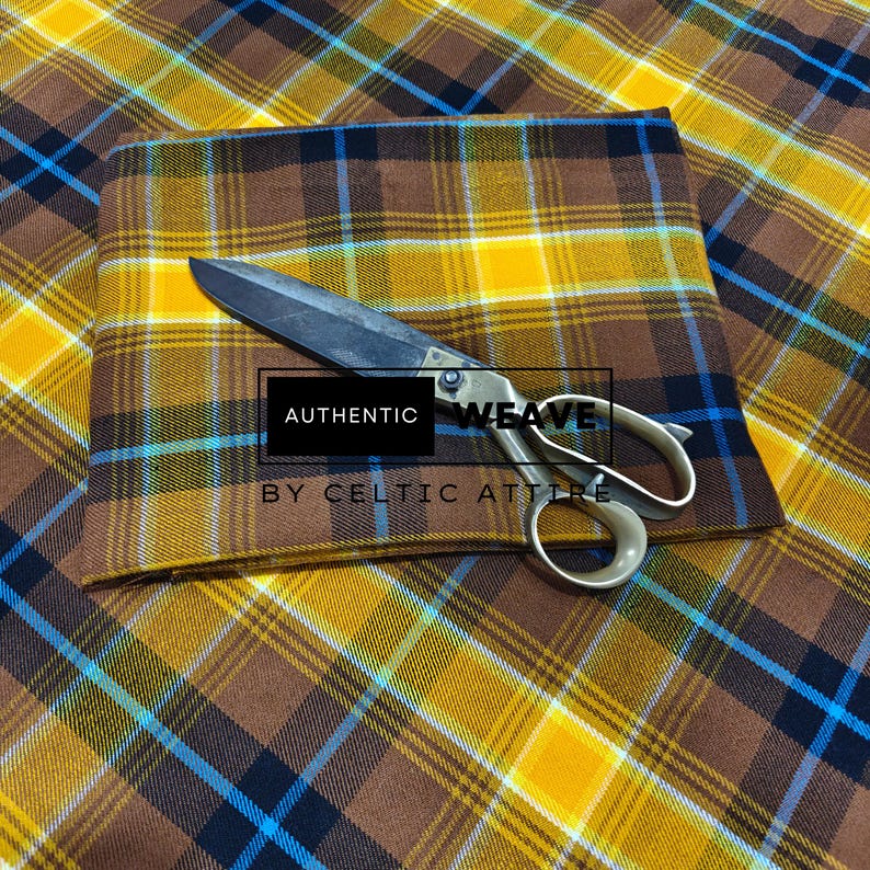K&ouml;nnte beinhalten: Ein gefalteter Stoff mit Karomuster in Braun-, Gelb- und Blaut&ouml;nen, mit einer offenen Schere darauf. Der Stoff hat ein klassisches Tartanmuster. Der Text "AUTHENTIC WEAVE BY CELTIC ATTIRE" ist sichtbar.