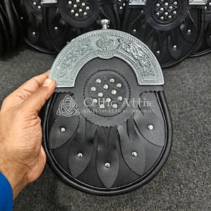 Pu&ograve; includere: Sporran in pelle nera con una parte superiore decorativa in metallo color argento. Lo sporran presenta un motivo a nodo celtico ed &egrave; impreziosito da borchie argentate. Il testo "Celtic Attire" &egrave; visibile.