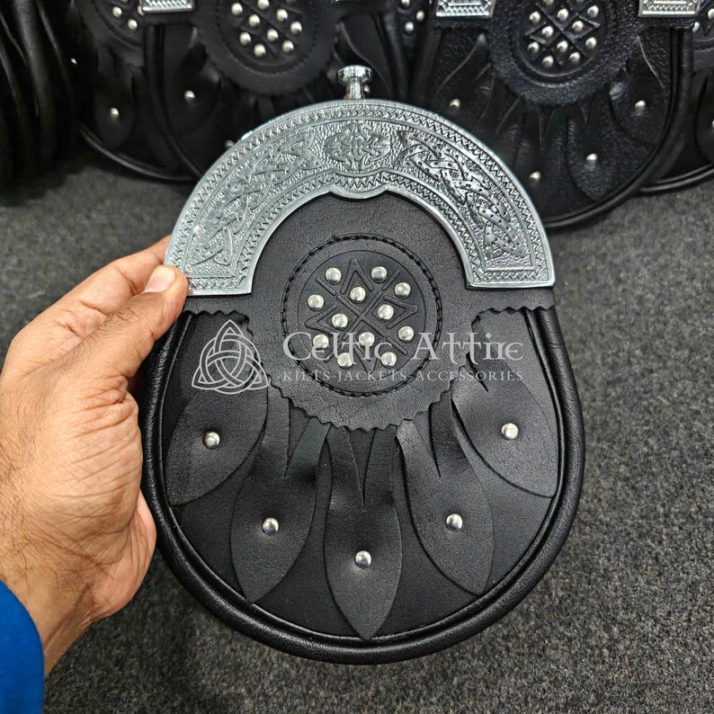 Pu&ograve; includere: Sporran in pelle nera con una parte superiore decorativa in metallo color argento. Lo sporran presenta un motivo a nodo celtico ed &egrave; impreziosito da borchie argentate. Il testo "Celtic Attire" &egrave; visibile.