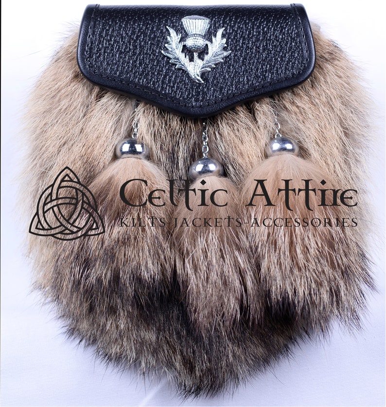 May include: A black leather sporran with three brown fur tassels and a silver thistle badge. The sporran is decorated with a silver chain and has the text "Celtic Attire Kilts Jackets Accessories" printed below.
