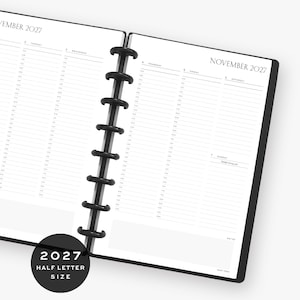 May include: A black disc-bound planner open to November 2027, featuring a weekly layout with hourly time slots from 6:00 to 8:00. The pages are white with black text, including the month and year, and a notes section at the bottom.