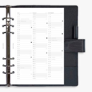 May include: A black leather planner with a silver binder and a calendar insert. The calendar pages are white with black text, displaying the months of July, August, and September. The planner is closed with a black strap.