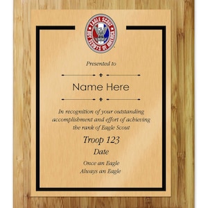 May include: A wooden plaque with a black border and a gold background. The plaque features the Boy Scouts of America Eagle Scout logo and text that reads "Presented to Name Here In recognition of your outstanding accomplishment and effort of achieving the rank of Eagle Scout Troop 123 Date Once an Eagle Always an Eagle"