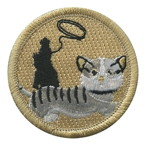 May include: Embroidered patch featuring a cartoon cat with gray and white stripes, a black silhouette, and a black lasso. The patch is circular with a gold border and a textured background.