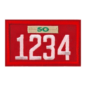 May include: A rectangular red embroidered patch with white numbers "1234" and the number "50" in green. The patch has a red border and a tan rectangle above the numbers.
