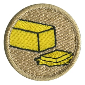 May include: A tan embroidered patch with a yellow stick of butter and a yellow pat of butter.