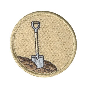 May include: A beige embroidered patch with a white shovel and brown dirt. The shovel has a brown handle.