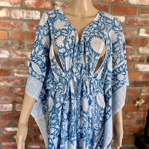 Puede incluir: Un vestido caftán con estampado floral azul y blanco con escote en V y mangas cortas. El vestido tiene cintura con cordón y un patrón geométrico blanco en los puños de las mangas. La tela tiene un diseño floral.