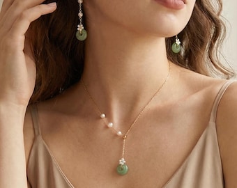 May include: A gold-tone necklace and matching drop earrings set featuring small white pearls and light green jade-style circular pendants. The necklace has an asymmetrical design with a dangling pendant, while the earrings feature a single drop.