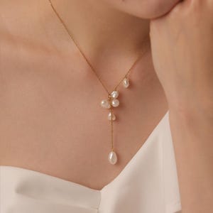 May include: A gold necklace with a cluster of white pearls. The necklace has a fine chain with a cascade of pearls, creating an elegant design. The pearls vary in size and shape, adding a unique touch to the jewellery. A stylish accessory.