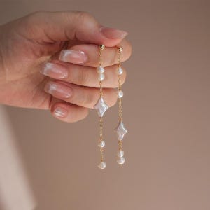 May include: A pair of gold earrings with a delicate chain and pearl accents. Each earring features a large, irregular shaped pearl.