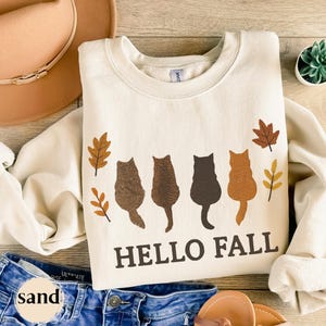Embroidered cats with “Hello Fall” text and autumn leaves design.