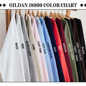 May include: A color chart displaying Gildan 18000 sweatshirts in various colors, including white, ash, sports grey, sand, light pink, light blue, carolina blue, navy, red, maroon, military green, forest green, dark chocolate, and black. The text "GILDAN 18000 COLOR CHART" is at the top.