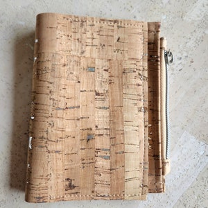 May include: A brown cork notebook with a zipper closure. The notebook has a natural cork texture and a subtle sheen.