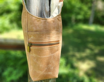 Puede incluir: Bolso de hombro de color marrón claro con un bolsillo frontal con cremallera y una cremallera de color bronce. El bolso cuelga de un poste de madera. Tiene una parte superior curvada y una correa de cadena con anillos decorativos.