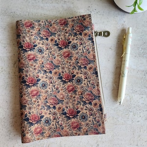 May include: A floral patterned zipped pouch with a beige background, featuring red and blue roses and other flowers. A white pen with floral accents rests beside the pouch. The pouch has a metal zip.