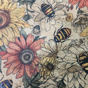 Op de afbeelding: Close-up van een bloemenpatroon met zonnebloemen, madeliefjes en andere bloemen in tinten geel, oranje en rood. Het ontwerp bevat illustraties van bijen. De achtergrond is lichtbeige.