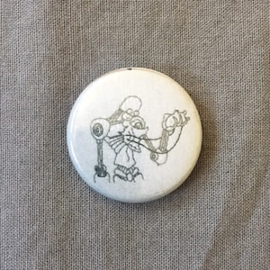 Può includere: Un bottone bianco con un disegno in bianco e nero di un robot con un occhio grande.