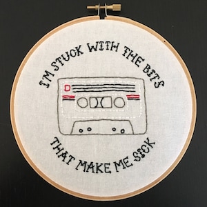 May include: White embroidery hoop with black thread embroidery of a cassette tape and the text "I'm stuck with the bits that make me sick".