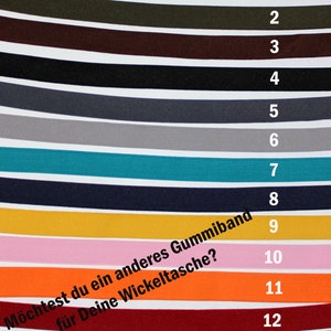 May include: Thirteen different colours of elastic bands, numbered 1 through 13. The text "M&ouml;chtest du ein anderes Gummiband f&uuml;r Deine Wickeltasche?" is written in black on a white background.