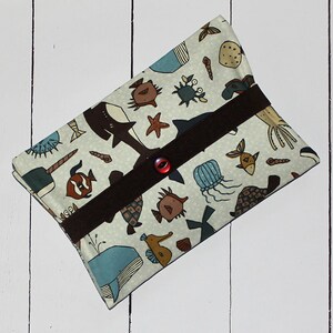 May include: A white fabric pouch with a brown strap and a red button closure. The pouch is decorated with a colourful sea life pattern, including fish, whales, jellyfish, and seahorses.