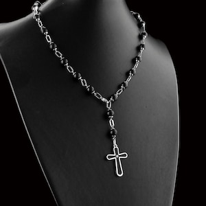 May include: A black beaded necklace with a silver cross pendant. The necklace is on a black display stand.