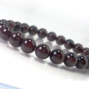 May include: A dark red gemstone bracelet with round beads. The bracelet is made of natural garnet stones.