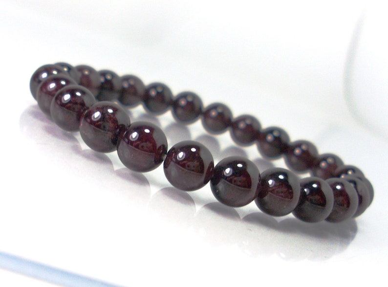 May include: A dark red gemstone bracelet with round beads. The bracelet is made of natural garnet stones.