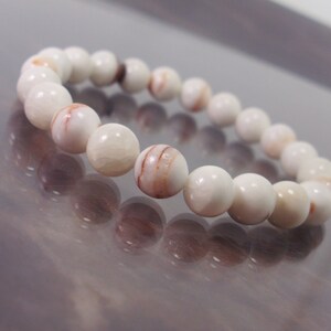 K&ouml;nnte beinhalten: Armband aus wei&szlig;en und rot gestreiften Edelsteinen. Das Armband besteht aus runden Perlen.